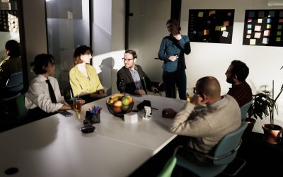 A group of businesspeople engages in a productive discussion in a stylish office with large windows. They share ideas around a table filled with refreshments, fostering collaboration.